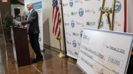 Blayne Primozich, EPCC associate vice president of workforce and continuing education, stands at a microphone. In the foreground is a giant, ceremonial check to EPCC for $100,000.