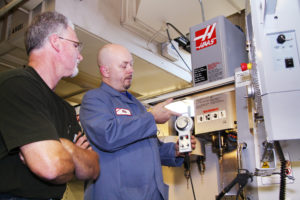 Two older white men at Bates Technical College--one a student, one a teacher--look at a manufacturing machine. One is intructing the other how to use it.