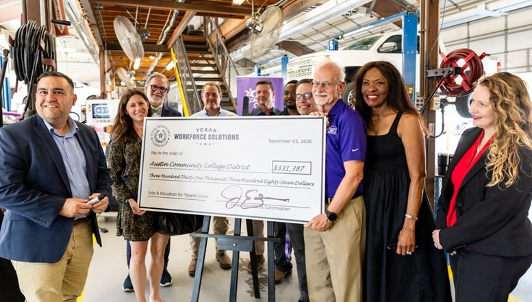 A group of people stands in a workshop setting, holding a large novelty check made out to the Austin Community College District for $331,887. The check is dated September 27, 2023, and is presented by Texas Workforce Solutions. The group includes men and women of diverse backgrounds, smiling and posing together. The workshop features various tools and equipment in the background, indicating a focus on vocational training or education.